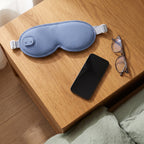 Blue eye mask and charging cable placed on a bedside table to show scale