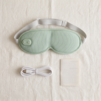 Green eye mask with its USB-C charging cable and English manual laid out on a linen surface